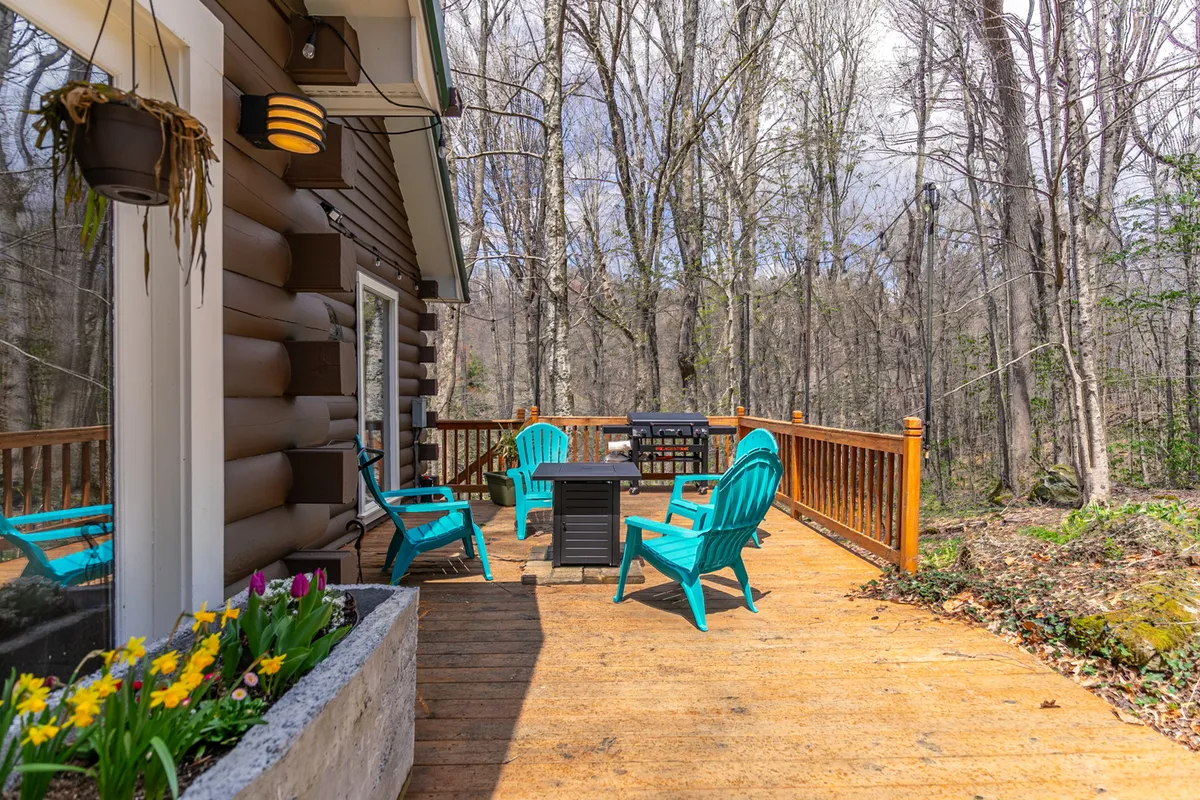 A tranquil wooden deck with blue chairs and an outdoor table, bordered by a vibrant flower planter. The inviting setup is ideal for socializing, relaxing, and watching sunsets together.