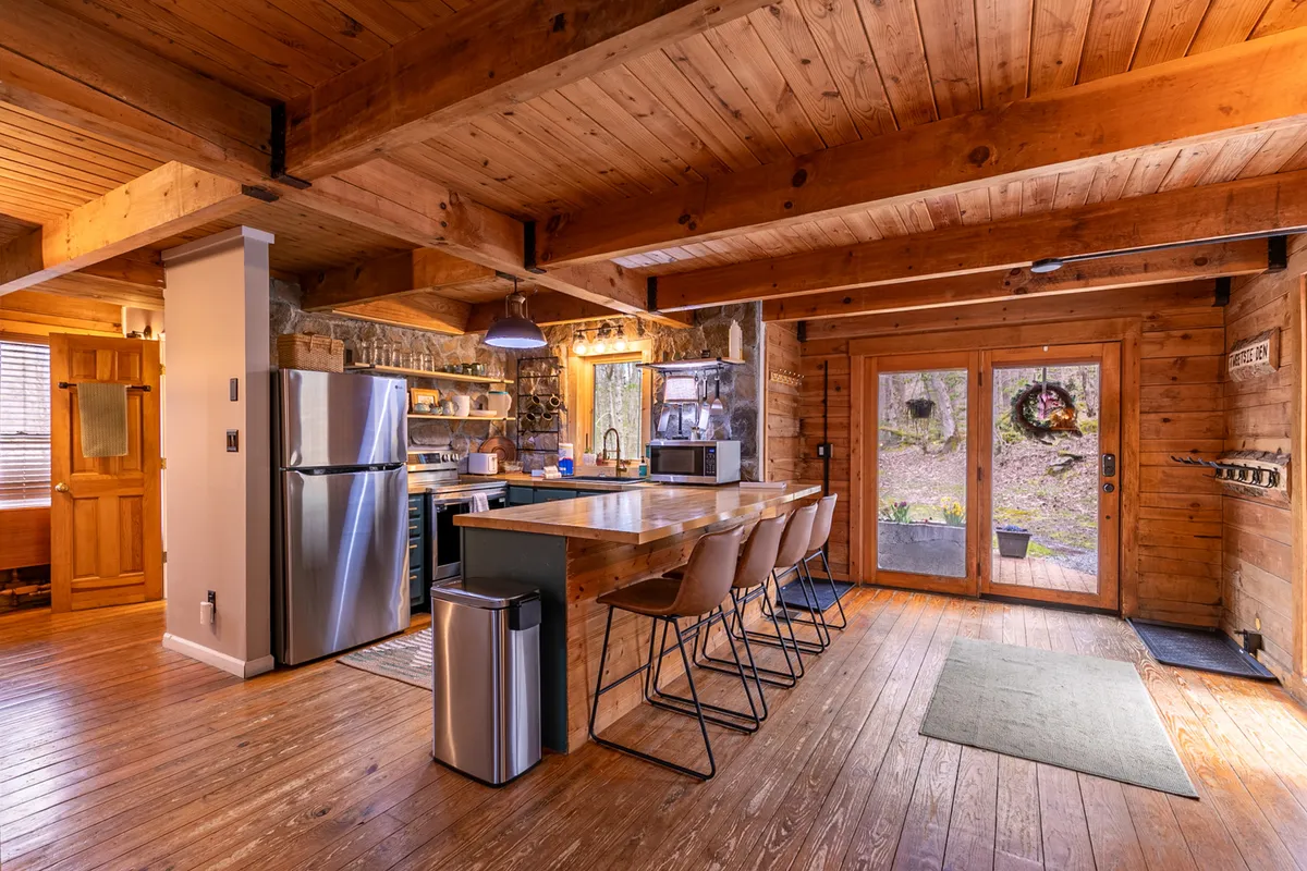 A welcoming kitchen with a large wooden countertop, stainless steel appliances, exposed beams, and sliding glass doors that open to nature. The kitchen island provides space for meals, conversation, and connection.