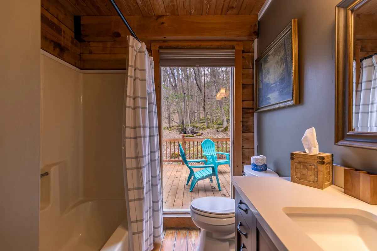 This image highlights a serene bathroom with a shower area, wooden deck access, and blue chairs positioned for enjoying the view. The sliding door and outdoor seating suggest stepping out directly into the mountain environment, inviting guests to start or end their day immersed in natural surroundings.